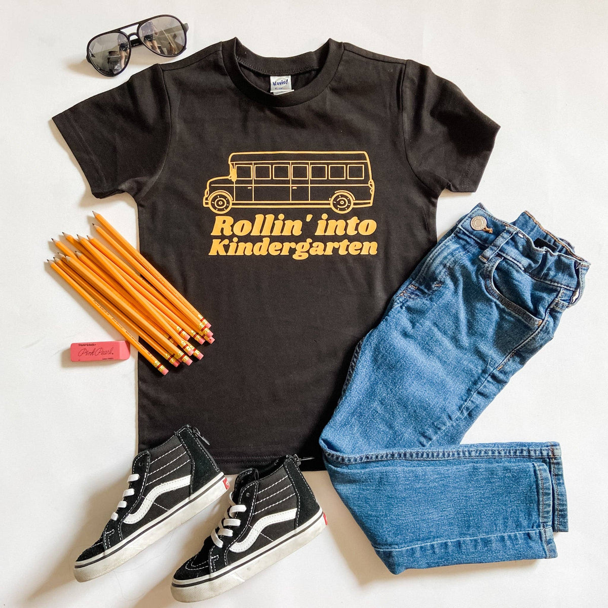 Rollin into Kindergarten black graphic tee, flat lay with school supplies