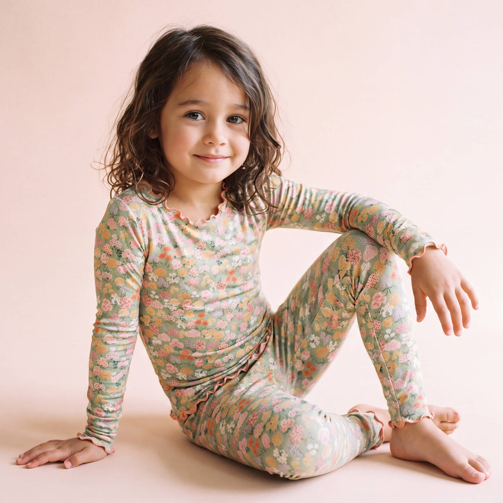 Field of Flowers bamboo lettuce-edge pajama set in sage green floral, worn by a girl sitting