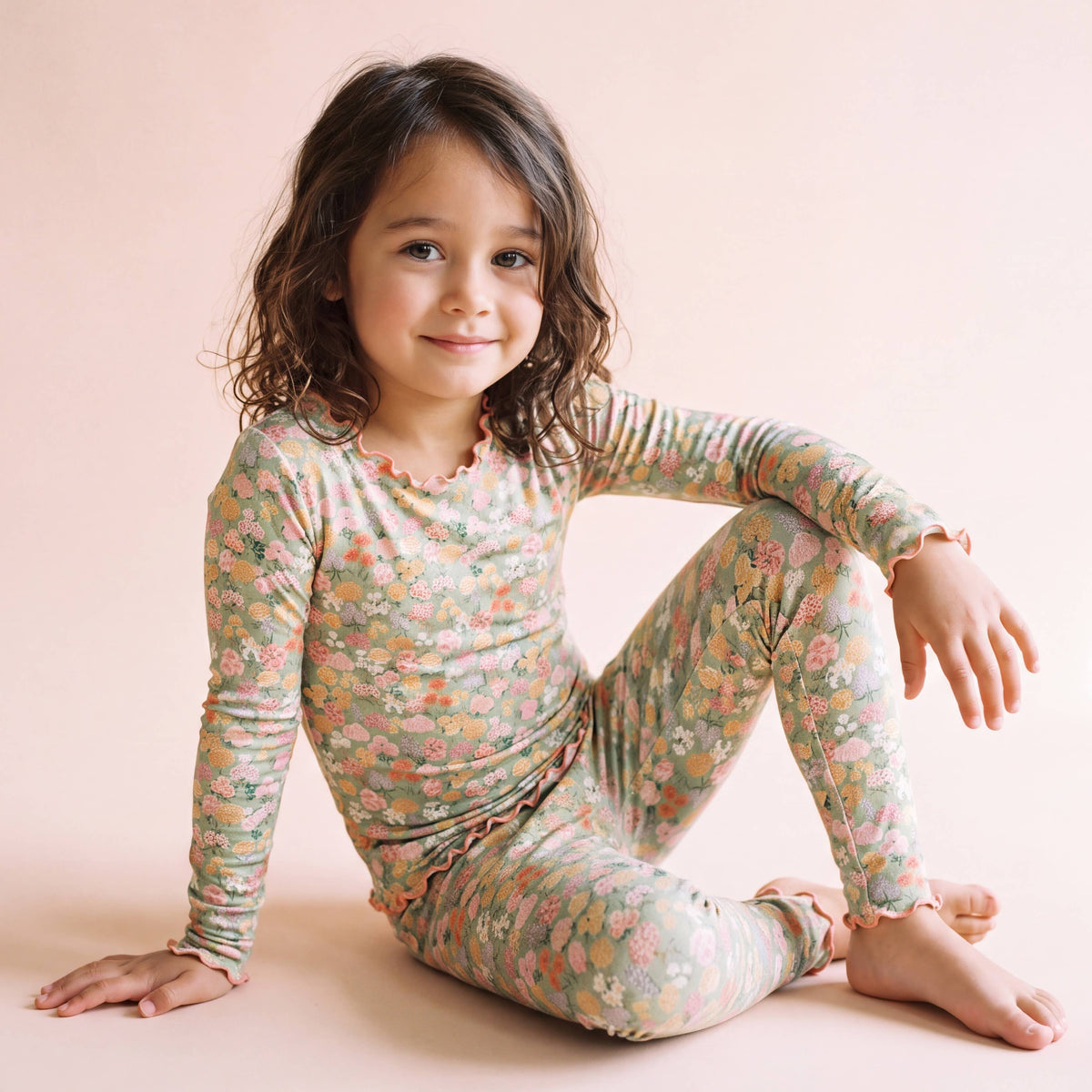 Field of Flowers bamboo lettuce-edge pajama set in sage green floral, worn by a girl sitting