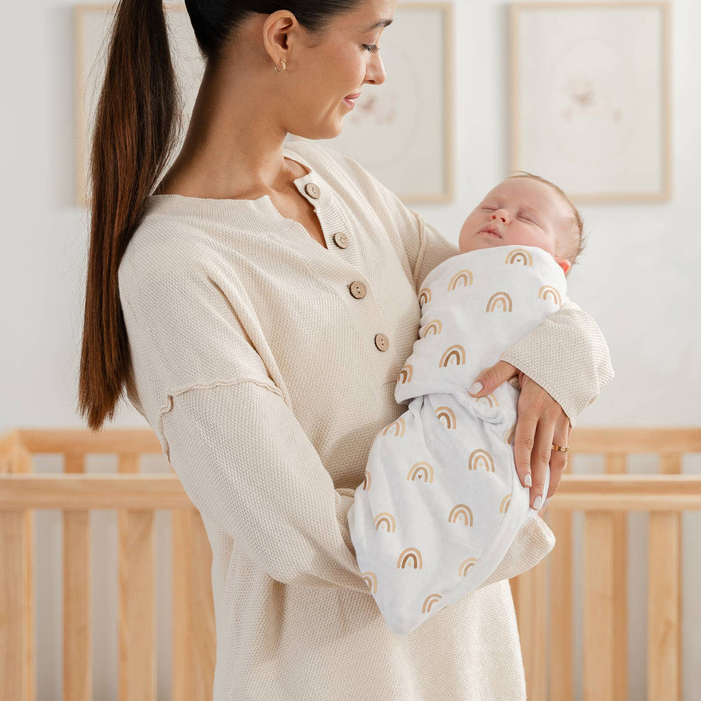 Mom holding a baby in the sand rainbow print easy swaddle