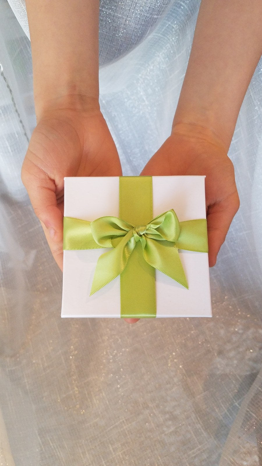 Hands holding a white gift box tied with a lime green satin bow