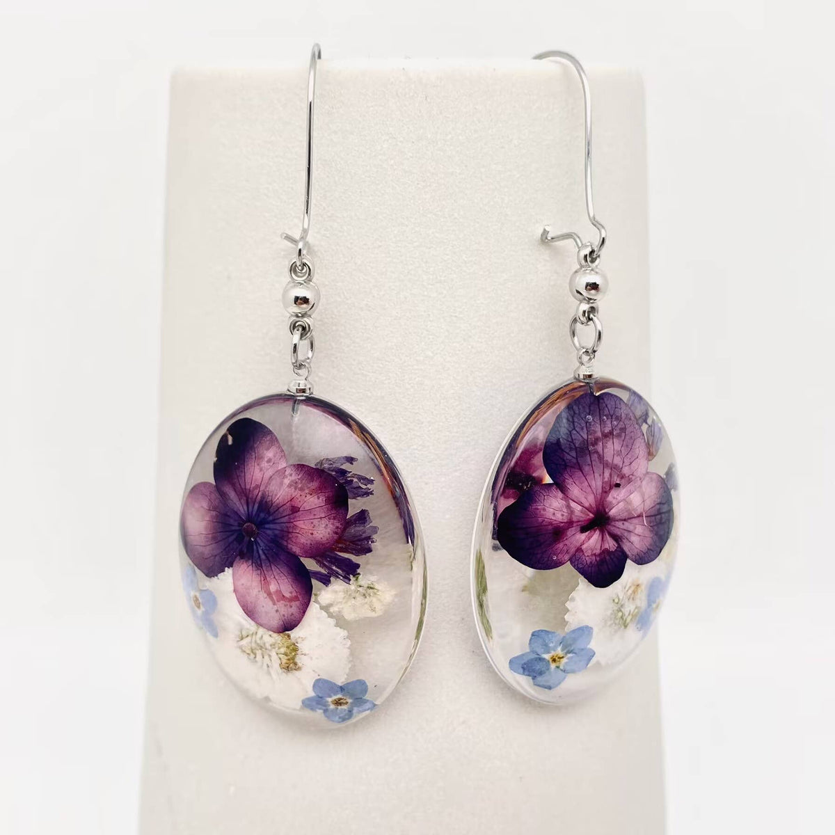 Purple, ivory and blue pressed flower oval dangle earrings, front view