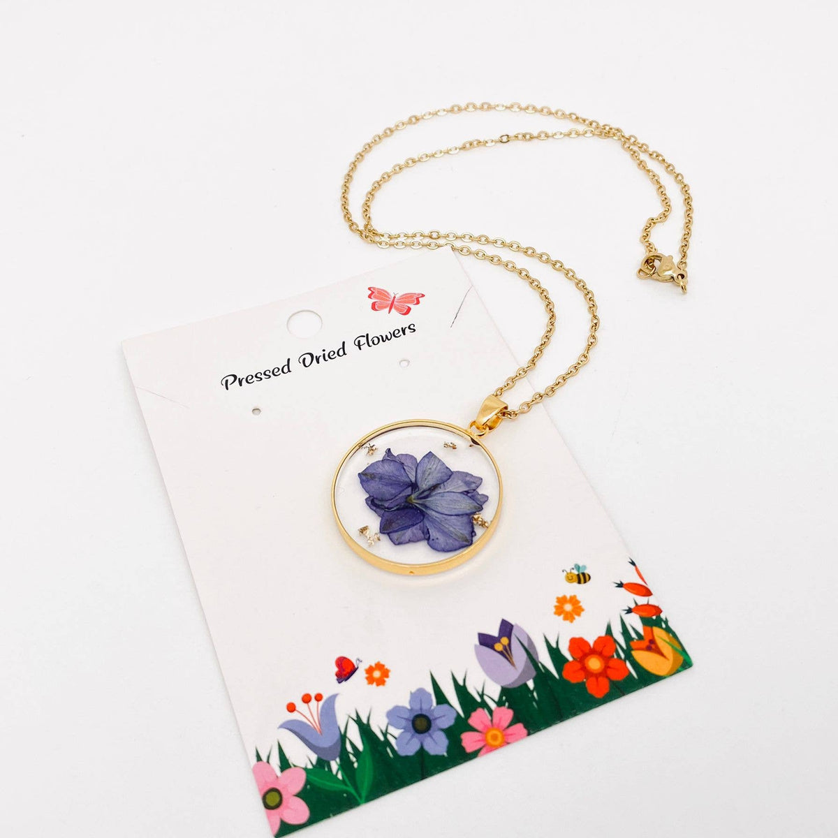 Purple pressed delphinium round pendant necklace, on its card with the chain
