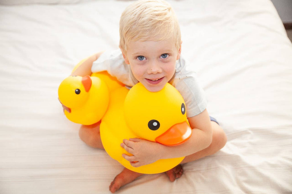Toddler hugging a giant yellow rubber duck on a bed