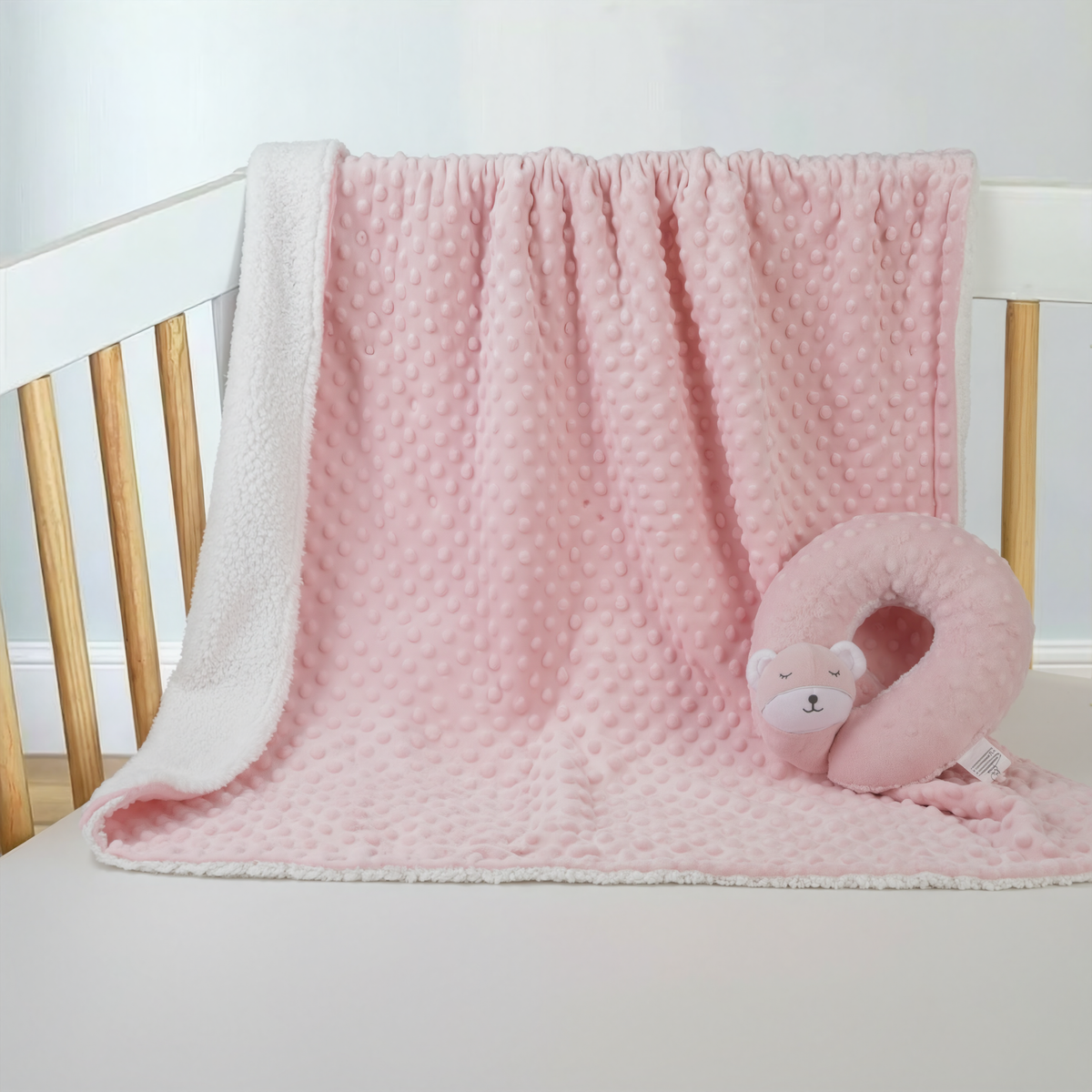 Pink minky dot baby blanket with sleepy bear neck pillow, in a crib with the pillow