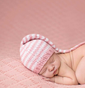 Newborn knit striped braided hat, pink and white, worn by sleeping baby