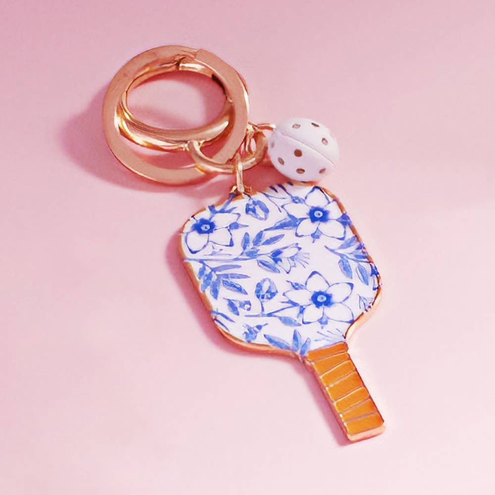 Blue and white floral pickleball paddle keychain bag charm, on a pink background