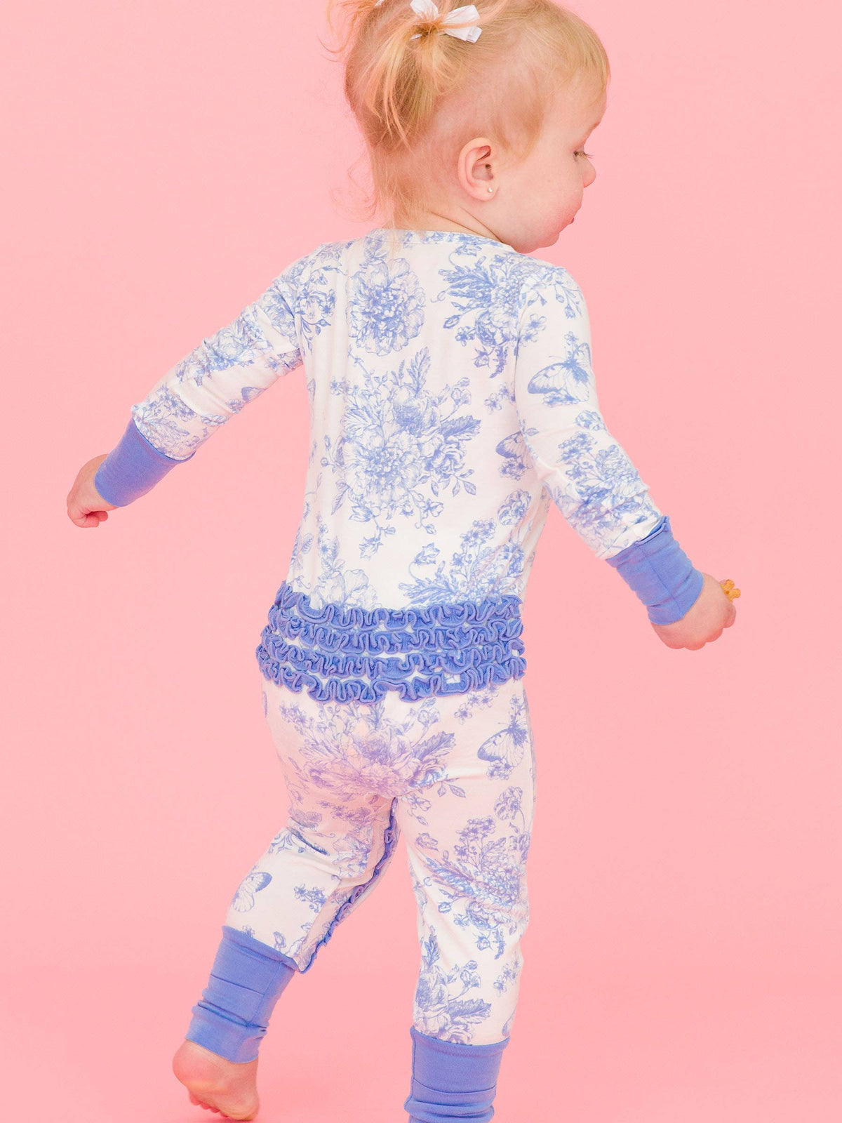 RuffleButts baby girl bamboo ruffled romper in periwinkle blue butterfly toile, on a toddler walking, back view