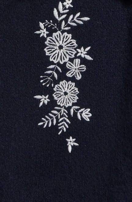 Close-up of the white floral embroidery on the navy sweater knit